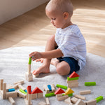 A child sat on a light grey coloured rug playing with the PlanToys 40 unit Colourful Block set. 
