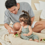 Young girl and man sat on a blanket playing with the PlanToys wooden baby car toy