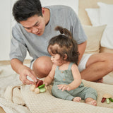 Young girl and man sat on a blanket playing with the PlanToys wooden baby car toy