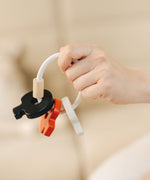 A close up of the PlanToys wooden baby key rattle toy in a high contrast colourway shown in an dult's hand. This baby toy has three wooden keys in white, red and black strung onto a white rope hoop. PlanToys range of toys are made from sustainably sourced rubberwood, we're proud stockists of PlanToys here at Babipur. 