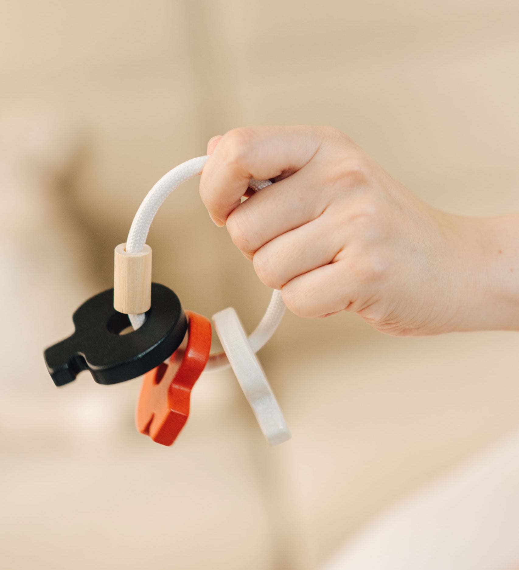 A close up of the PlanToys wooden baby key rattle toy in a high contrast colourway shown in an dult's hand. This baby toy has three wooden keys in white, red and black strung onto a white rope hoop. PlanToys range of toys are made from sustainably sourced rubberwood, we're proud stockists of PlanToys here at Babipur. 