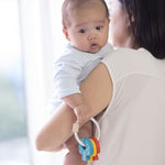 A baby being held by and adult, the baby is holding on to the PlanToys Baby Key Rattle. 