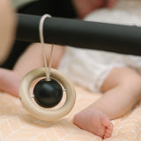 The black and whte planet hanging toy from the PlanToys High Contrast Wooden Baby Play Gym placed on teh bar of a pram. The wooden baby gym has high contrast coloured features and detailing. The gym comes with two wooden hanging toys, a planet and a rocket. PlanToys range of toys are made from sustainably sourced rubberwood, we're proud stockists of PlanToys here at Babipur. 