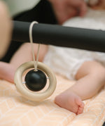 The black and whte planet hanging toy from the PlanToys High Contrast Wooden Baby Play Gym placed on teh bar of a pram. The wooden baby gym has high contrast coloured features and detailing. The gym comes with two wooden hanging toys, a planet and a rocket. PlanToys range of toys are made from sustainably sourced rubberwood, we're proud stockists of PlanToys here at Babipur. 