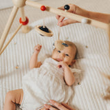 A baby laying underneath the PlanToys High Contrast Wooden Baby Play Gym looking up at the high contrast hanging toys as a. This wooden baby gym has high contrast coloured features and detailing. The gym comes with two wooden hanging toys, a planet and a rocket. PlanToys range of toys are made from sustainably sourced rubberwood, we're proud stockists of PlanToys here at Babipur.  adult placed one of the toys on the gym