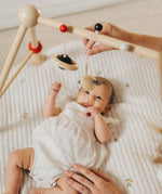 A baby laying underneath the PlanToys High Contrast Wooden Baby Play Gym looking up at the high contrast hanging toys as a. This wooden baby gym has high contrast coloured features and detailing. The gym comes with two wooden hanging toys, a planet and a rocket. PlanToys range of toys are made from sustainably sourced rubberwood, we're proud stockists of PlanToys here at Babipur.  adult placed one of the toys on the gym