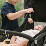 A young child standing near a pushchair holding up the rocket shaped wooden toy from the PlanToys High Contrast Wooden Baby Play Gym with a baby laying underneath . The wooden baby gym has high contrast coloured features and detailing. The gym comes with two wooden hanging toys, a planet and a rocket. PlanToys range of toys are made from sustainably sourced rubberwood, we're proud stockists of PlanToys here at Babipur. 