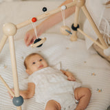 A baby laying underneath the PlanToys High Contrast Wooden Baby Play Gym looking up at the high contrast hanging toys. This wooden baby gym has high contrast coloured features and detailing. The gym comes with two wooden hanging toys, a planet and a rocket. PlanToys range of toys are made from sustainably sourced rubberwood, we're proud stockists of PlanToys here at Babipur. 