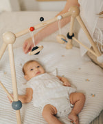 A baby laying underneath the PlanToys High Contrast Wooden Baby Play Gym looking up at the high contrast hanging toys. This wooden baby gym has high contrast coloured features and detailing. The gym comes with two wooden hanging toys, a planet and a rocket. PlanToys range of toys are made from sustainably sourced rubberwood, we're proud stockists of PlanToys here at Babipur. 