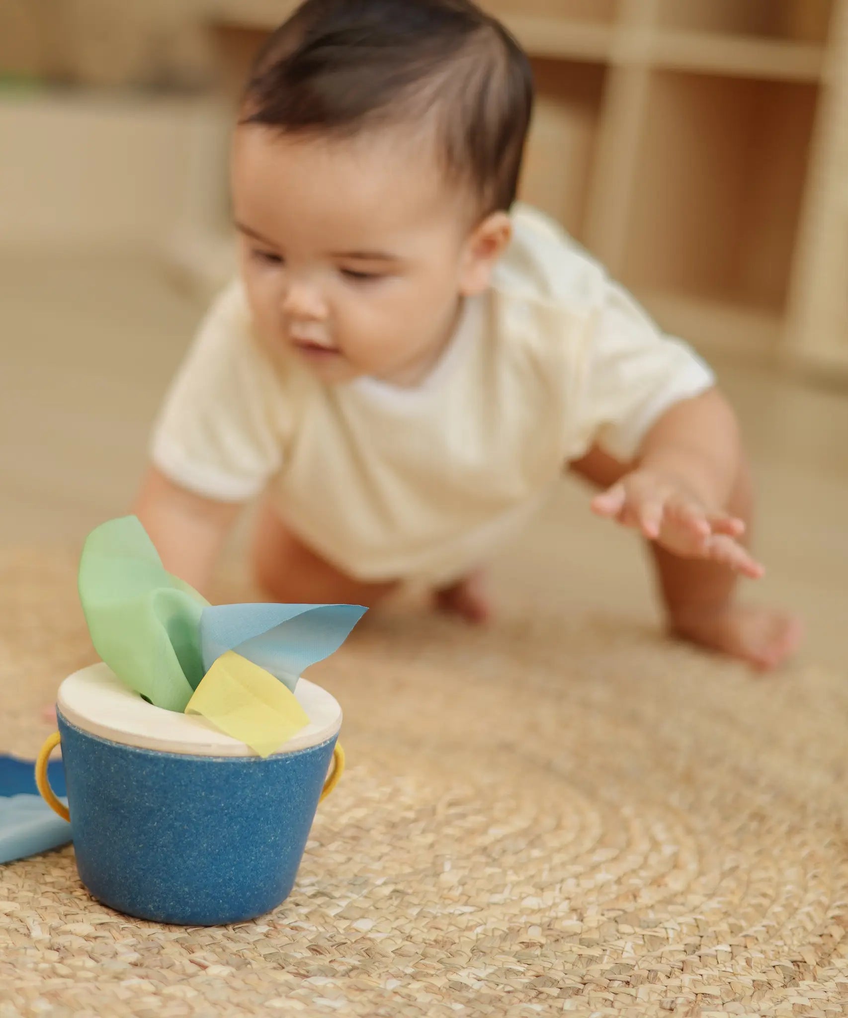 Baby crawling towards the PlanToys baby tissue box wooden sensory toy.