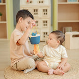 Child holding the PlanToys baby tissue box wooden sensory toy in front of a baby whilst the baby reaches for the material sticking out.