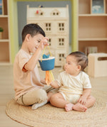 Child holding the PlanToys baby tissue box wooden sensory toy in front of a baby whilst the baby reaches for the material sticking out.