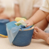 Close up of a baby's hands pulling material out of the PlanToys baby tissue box wooden sensory toy.