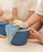 Close up of a baby's hands pulling material out of the PlanToys baby tissue box wooden sensory toy.