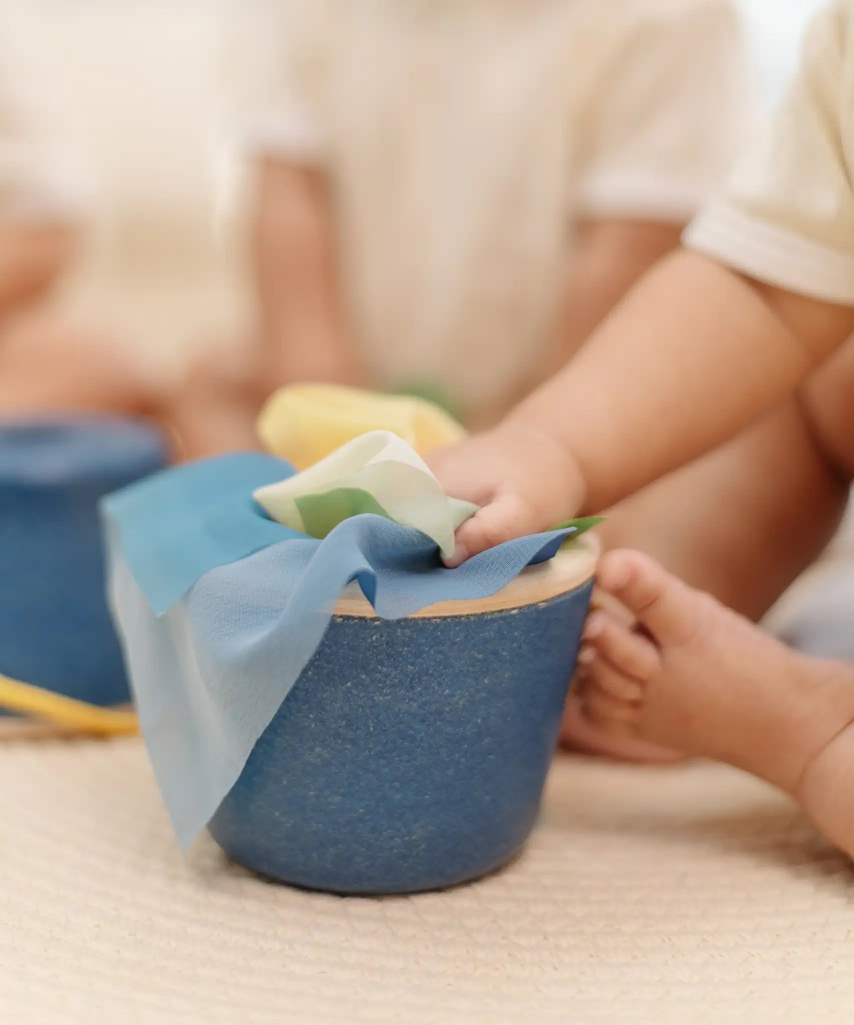 Close up of a baby's hands pulling material out of the PlanToys baby tissue box wooden sensory toy.