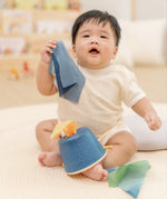 Baby pulling blue material out of the PlanToys baby tissue box wooden sensory toy.