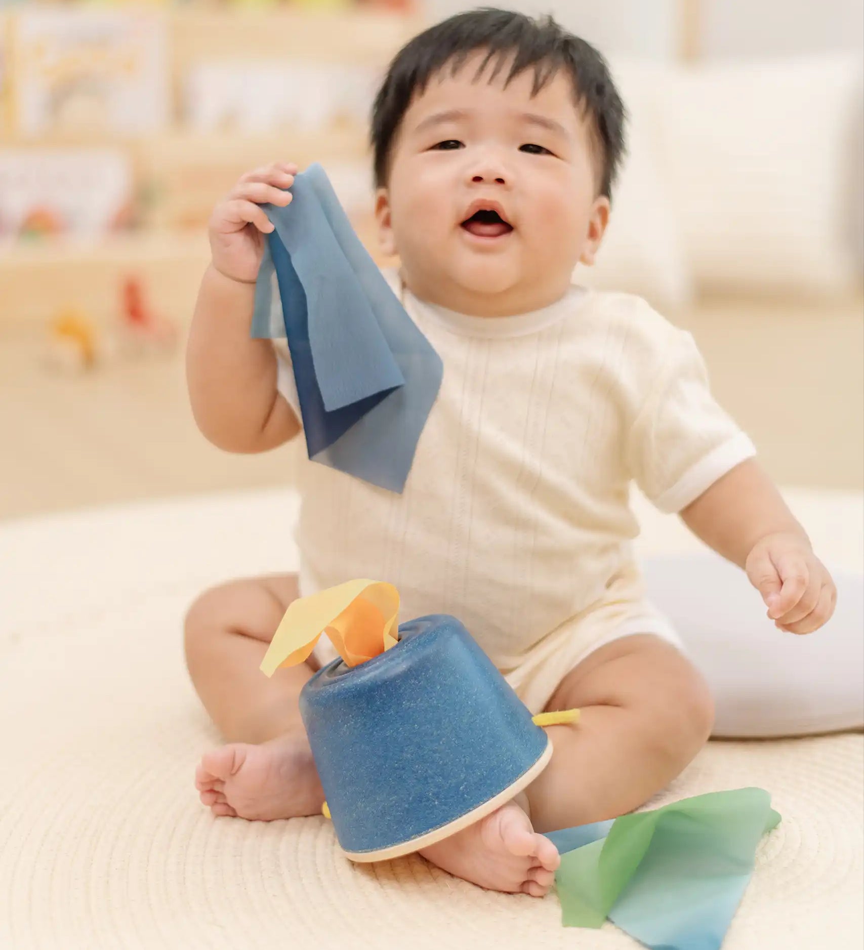 Baby pulling blue material out of the PlanToys baby tissue box wooden sensory toy.