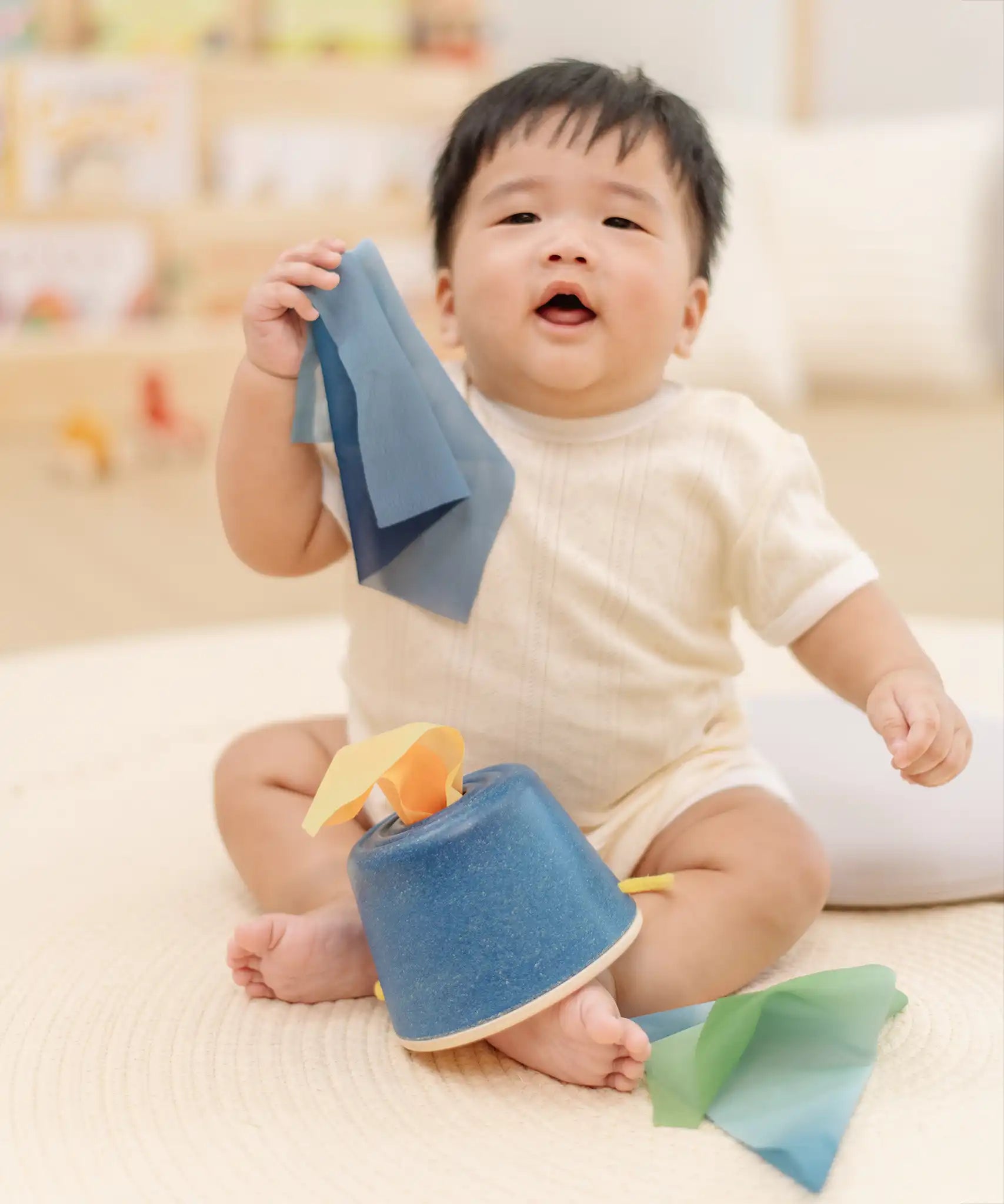 Baby pulling blue material out of the PlanToys baby tissue box wooden sensory toy.
