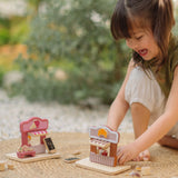 Child playing with the PlanToys bakery shop wooden toy playset with the ice cream shop playset placed besides it.