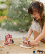 Child playing with the PlanToys bakery shop wooden toy playset with the ice cream shop playset placed besides it.