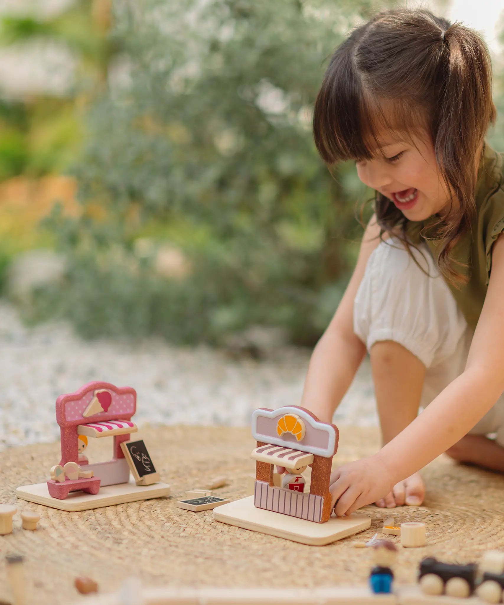 Child playing with the PlanToys bakery shop wooden toy playset with the ice cream shop playset placed besides it.