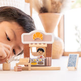 Child playing with the PlanToys bakery shop wooden toy playset, placing baking tools into a pot.