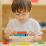 Child placing blocks on the PlanToys balancing cargo wooden balance game. Stack of wooden blocks balanced on a base piece placed on an upturned arch piece.