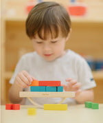 Child placing blocks on the PlanToys balancing cargo wooden balance game. Stack of wooden blocks balanced on a base piece placed on an upturned arch piece.