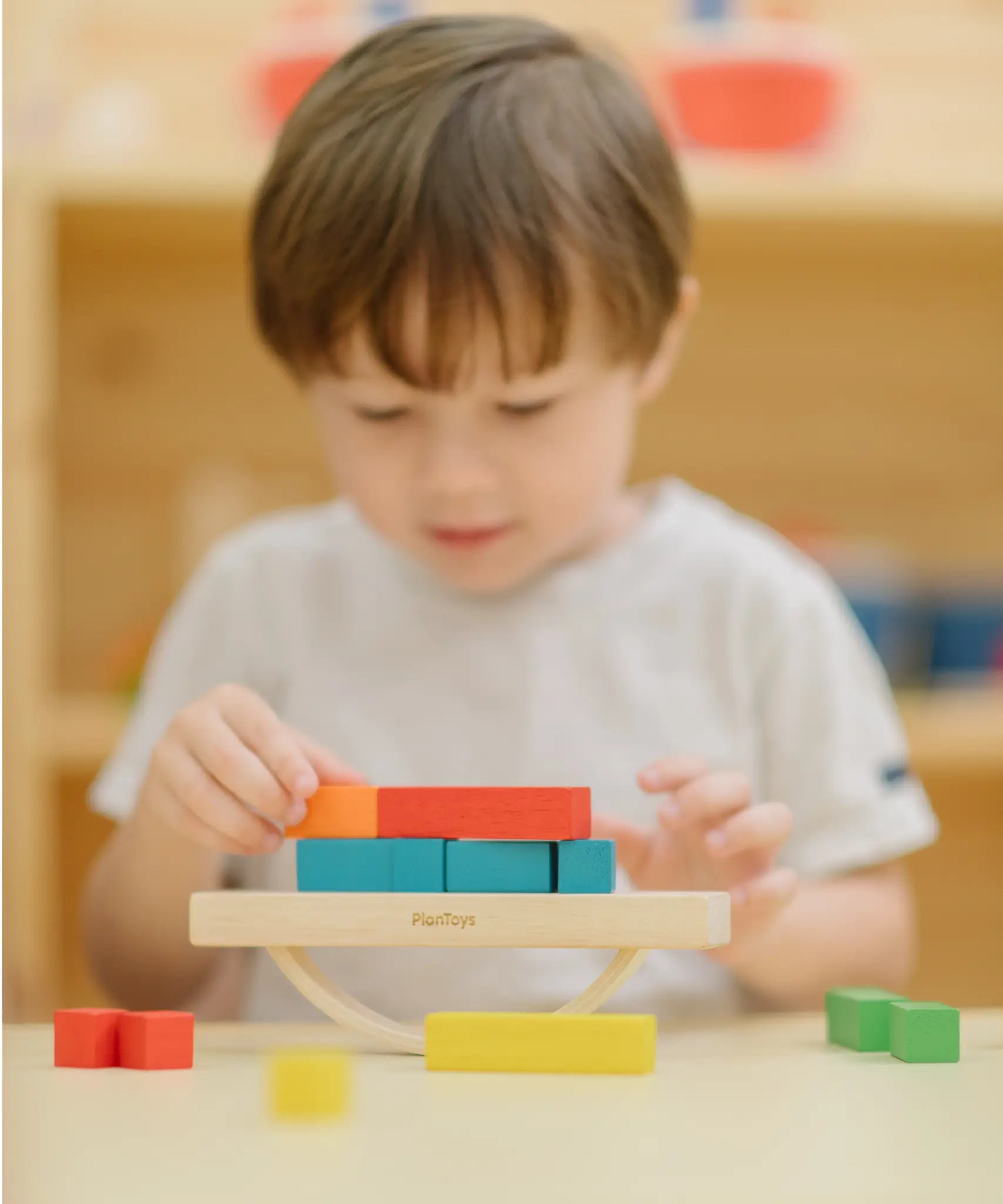 Child placing blocks on the PlanToys balancing cargo wooden balance game. Stack of wooden blocks balanced on a base piece placed on an upturned arch piece.