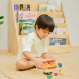 Child placing blocks on the PlanToys balancing cargo wooden balance game. Stack of wooden blocks balanced on a base piece placed on an upturned arch piece.