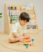 Child placing blocks on the PlanToys balancing cargo wooden balance game. Stack of wooden blocks balanced on a base piece placed on an upturned arch piece.