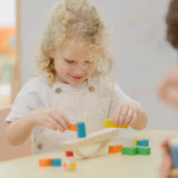 Child placing blocks on the PlanToys balancing cargo wooden balance game. Stack of wooden blocks balanced on a base piece placed on an upturned arch piece.