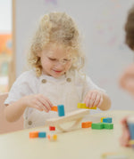 Child placing blocks on the PlanToys balancing cargo wooden balance game. Stack of wooden blocks balanced on a base piece placed on an upturned arch piece.