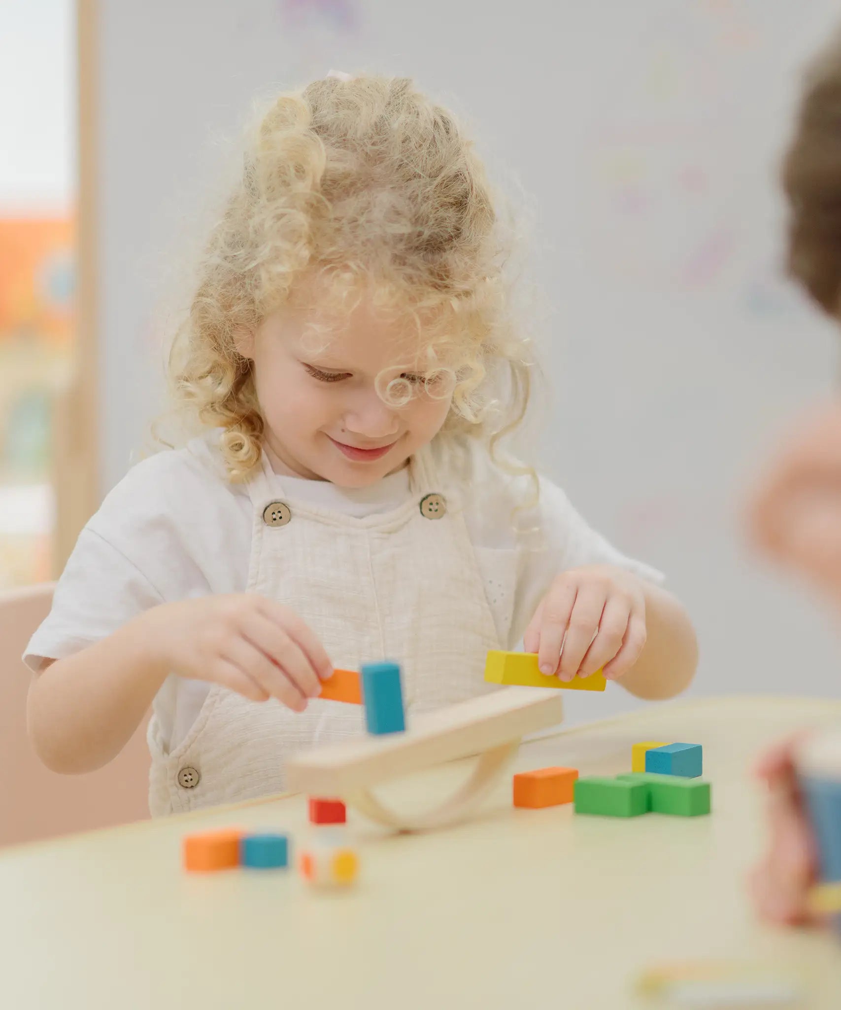 Child placing blocks on the PlanToys balancing cargo wooden balance game. Stack of wooden blocks balanced on a base piece placed on an upturned arch piece.