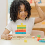 Child playing with the PlanToys balancing cargo wooden balance game. Holding the base piece with a stack of colourful wooden blocks balanced on the base piece.