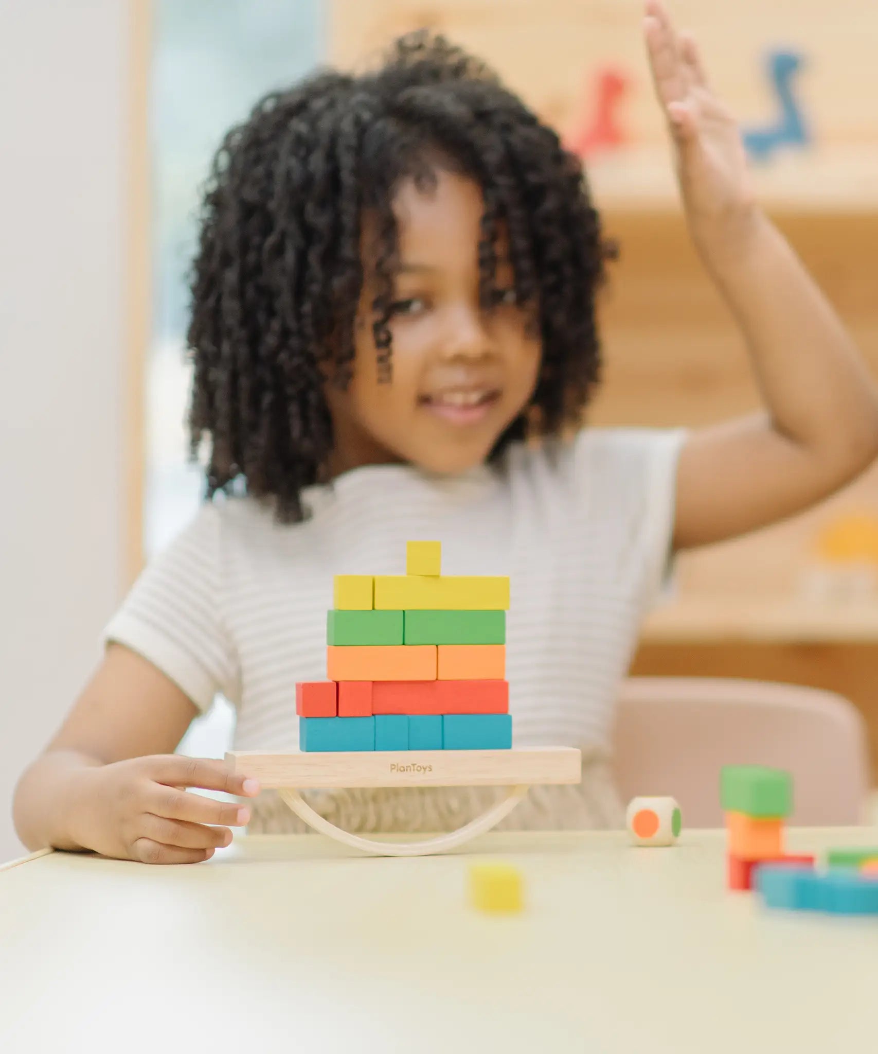 Child playing with the PlanToys balancing cargo wooden balance game. Holding the base piece with a stack of colourful wooden blocks balanced on the base piece.