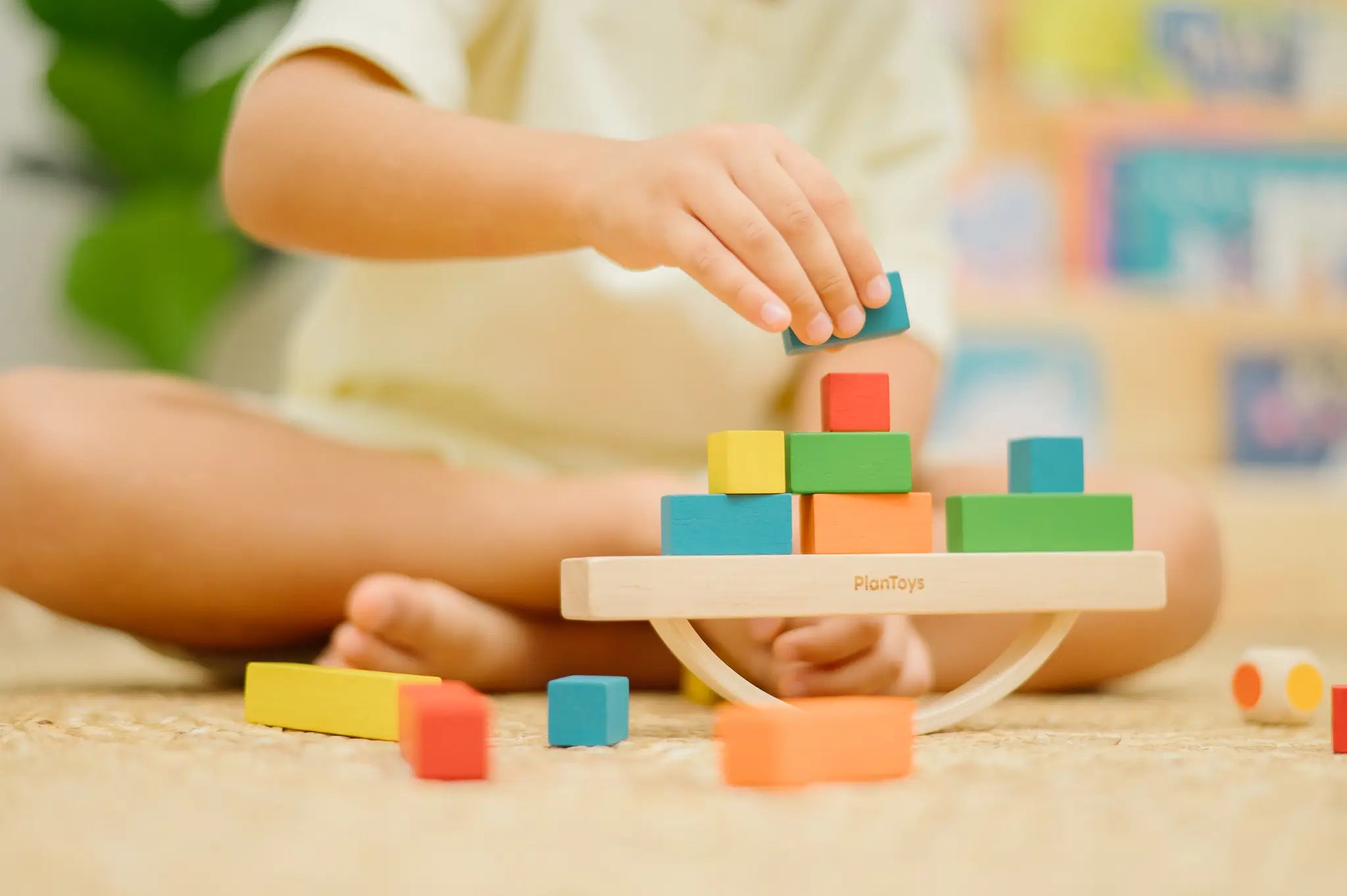 Child placing blocks on the PlanToys balancing cargo wooden balance game. Stack of wooden blocks balanced on a base piece placed on an upturned arch piece.