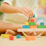 Child placing blocks on the PlanToys balancing cargo wooden balance game. Stack of wooden blocks balanced on a base piece placed on an upturned arch piece.