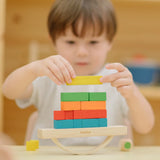 Child placing blocks on the PlanToys balancing cargo wooden balance game. Stack of wooden blocks balanced on a base piece placed on an upturned arch piece.
