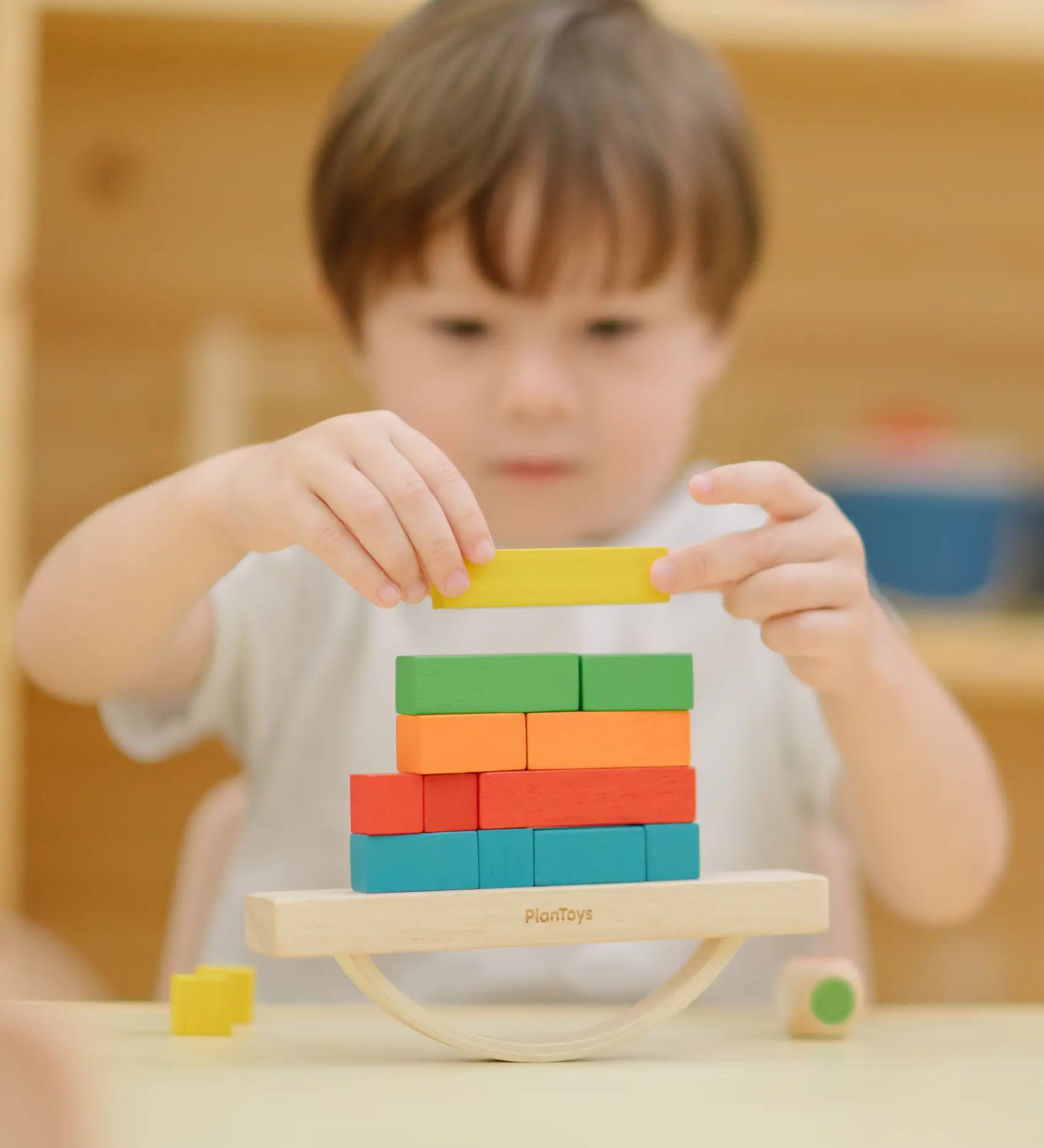 Child placing blocks on the PlanToys balancing cargo wooden balance game. Stack of wooden blocks balanced on a base piece placed on an upturned arch piece.