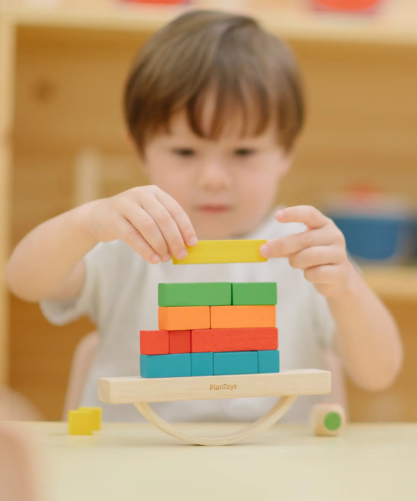 Child placing blocks on the PlanToys balancing cargo wooden balance game. Stack of wooden blocks balanced on a base piece placed on an upturned arch piece.
