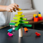 A close up of a child's hand placing the yellow coloured bird figures on the top of the Plan Toys Balancing Tree.
