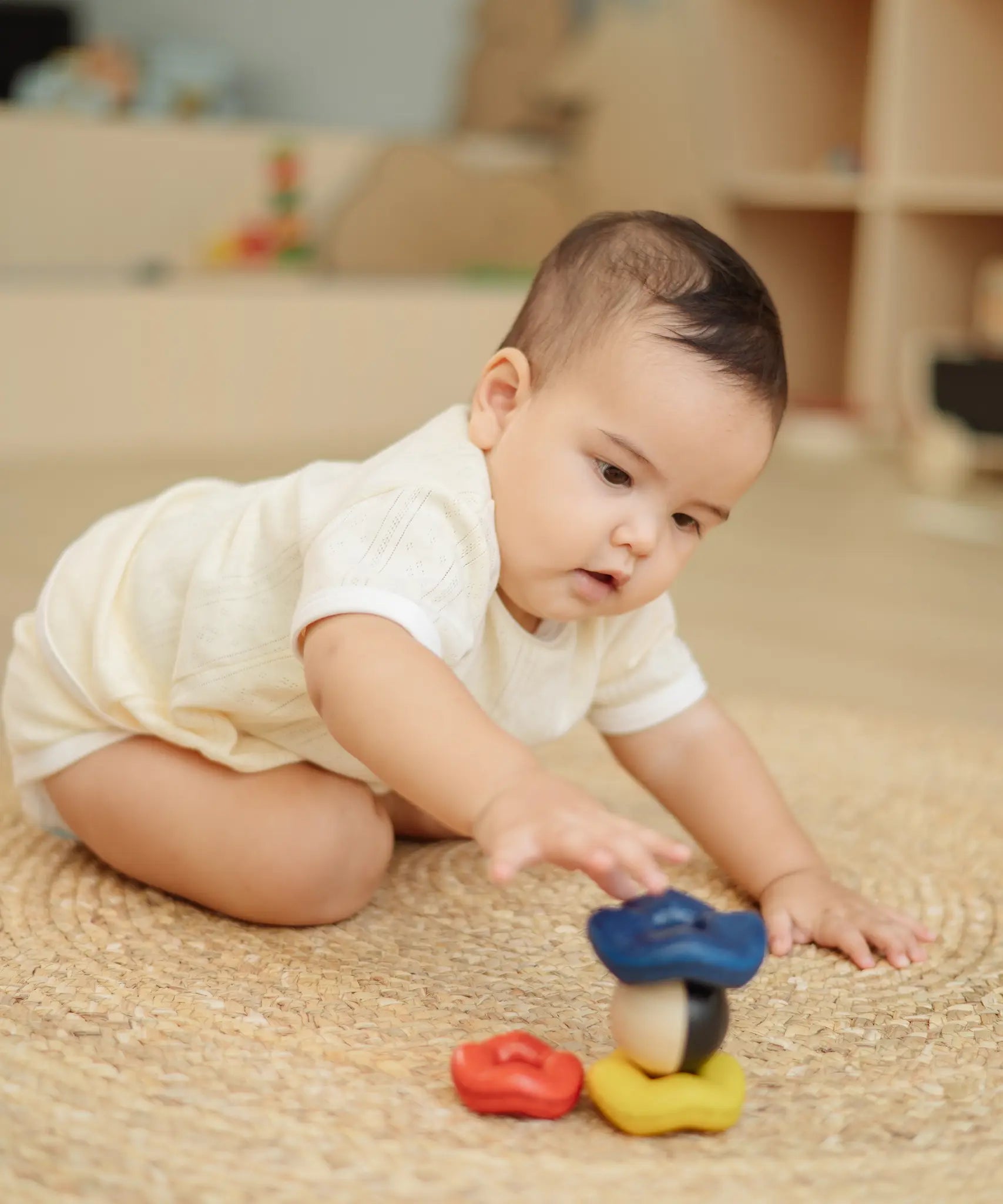 Baby playing with the PlanToys ball and wave stacker wooden baby stacking toy reaching for the stack