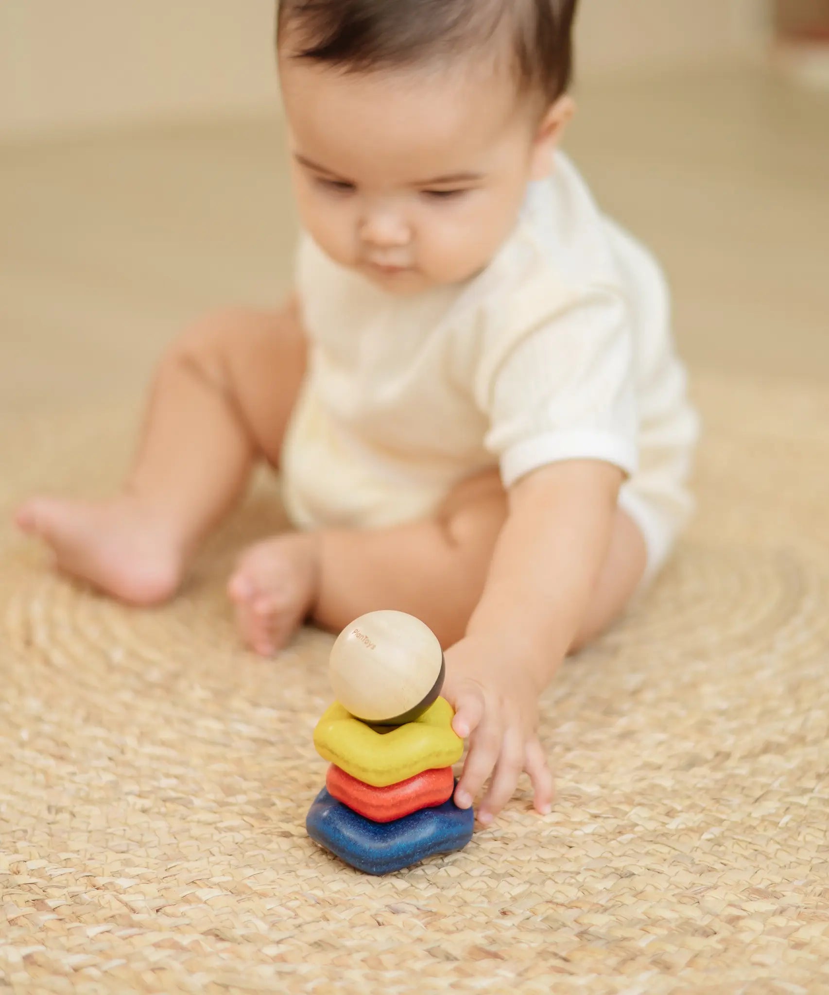 Baby playing with the PlanToys ball and wave stacker wooden baby stacking toy reaching for the stack.