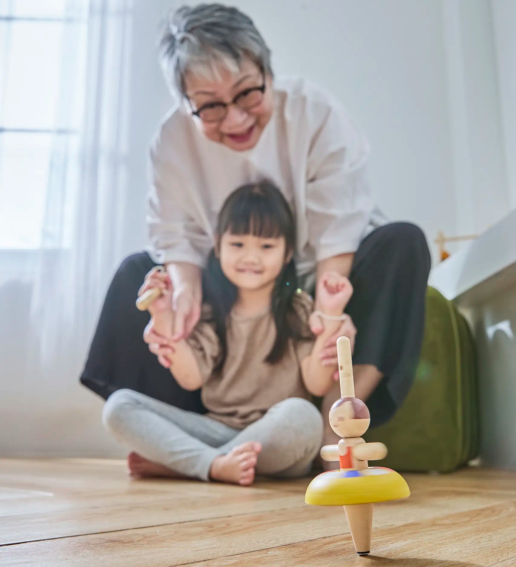 Child and grandmother playing with the PlanToys ballet spinning top on the floor 