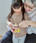 Grandmother and child threading the string on the handle of the Plantoys ballet spinning top 
