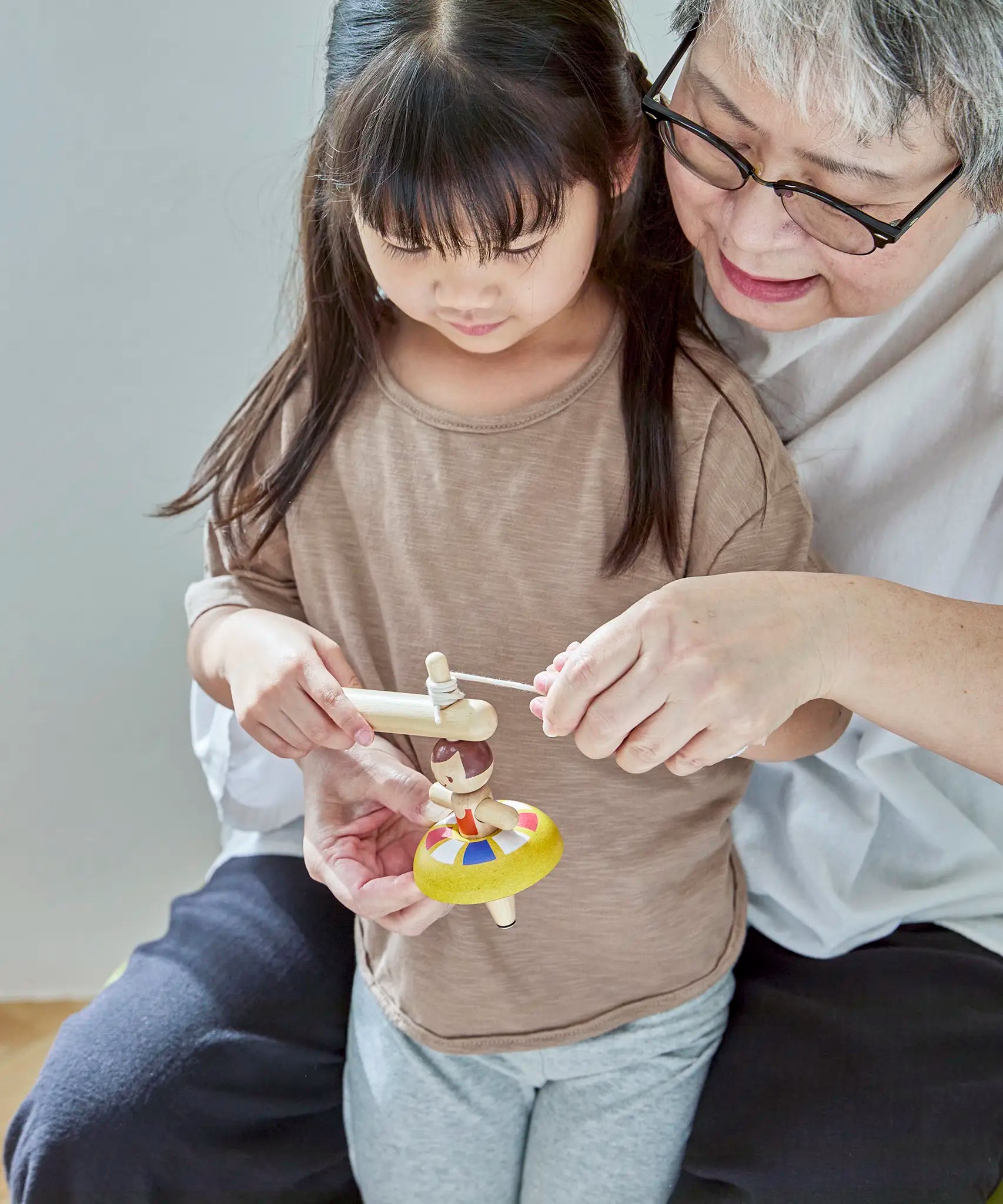 Grandmother and child threading the string on the handle of the Plantoys ballet spinning top 