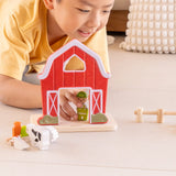 Child playing with the PlanToys barn house small world play set, holding the farmer figure placing it by the door of the barn. 