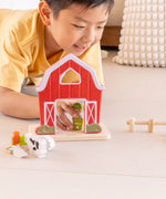 Child playing with the PlanToys barn house small world play set, holding the farmer figure placing it by the door of the barn. 