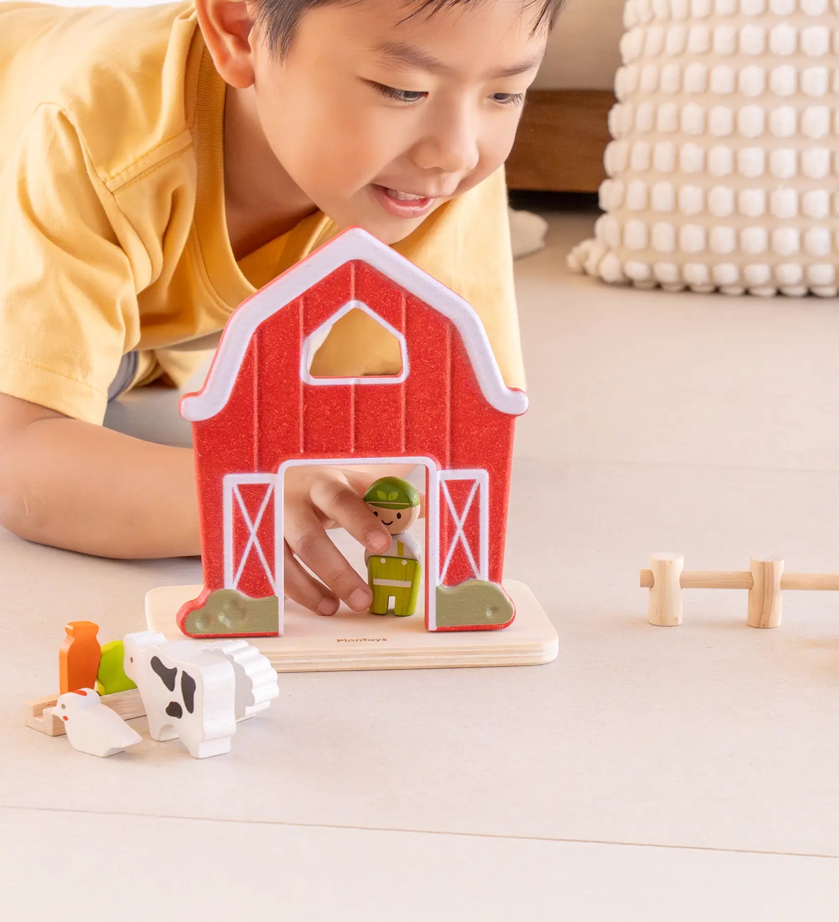 Child playing with the PlanToys barn house small world play set, holding the farmer figure placing it by the door of the barn. 